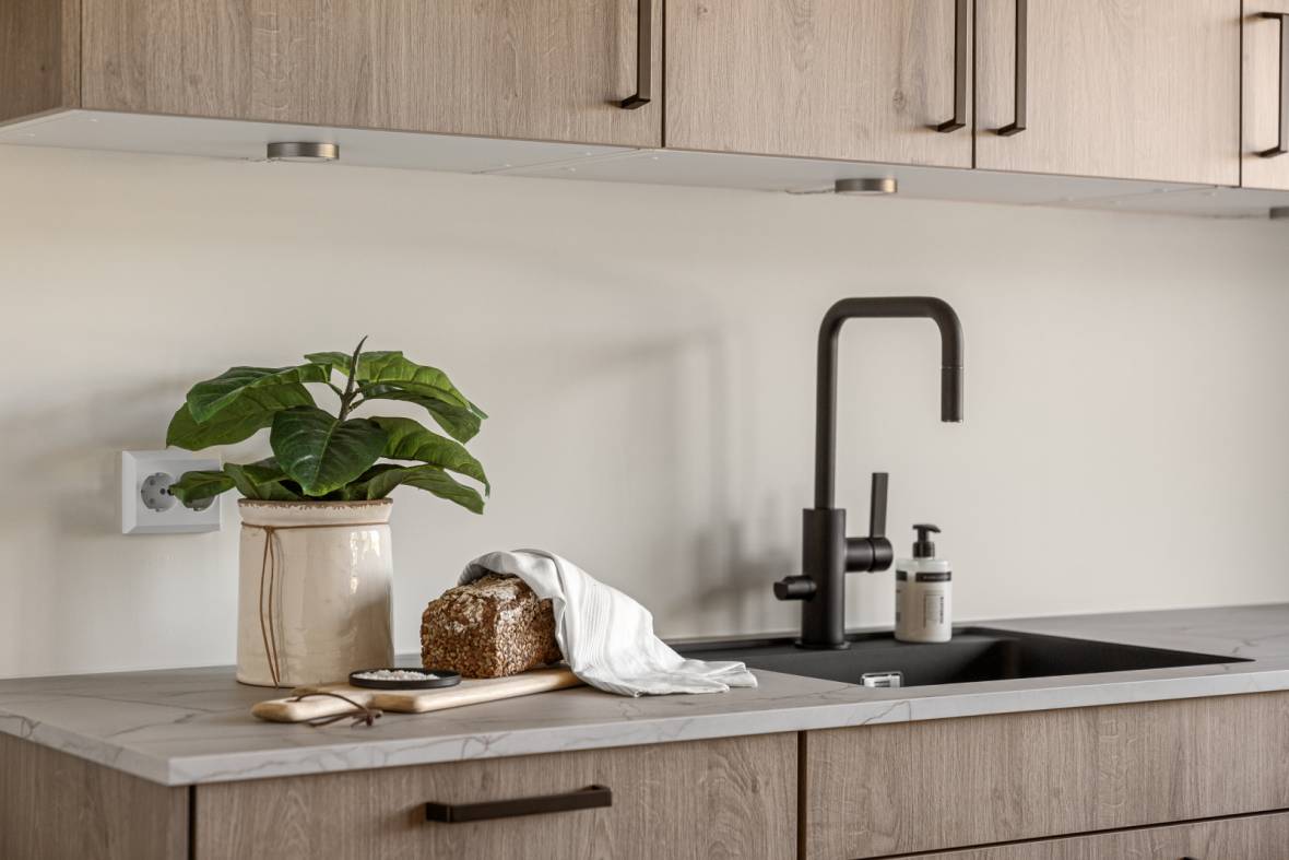 Stylet kjøkkenbenk i nybygg med trekjøkken og grønn plante